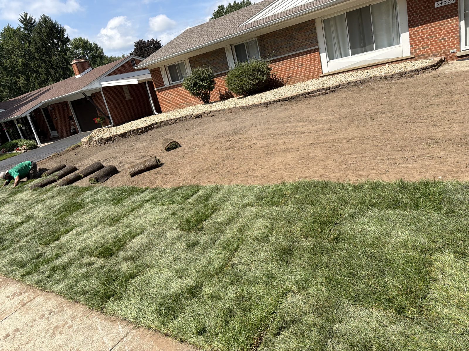 Bare graded soil with sod rolls being laid during a new lawn installation in Rochester, MI